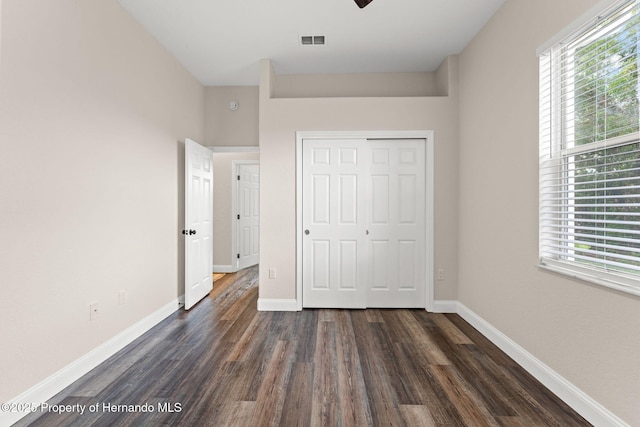 unfurnished bedroom with dark wood finished floors, baseboards, and a closet