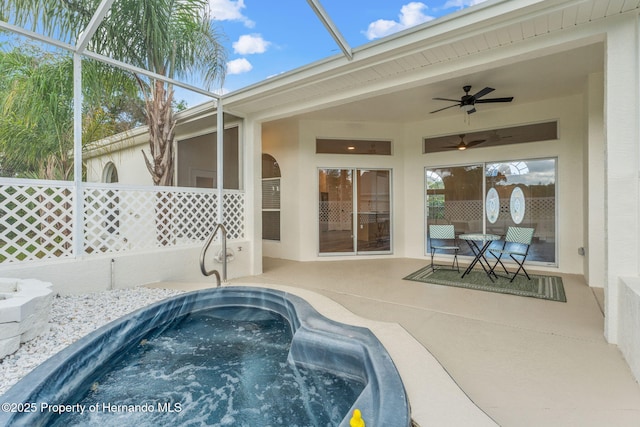 view of pool featuring ceiling fan, a patio, an outdoor hot tub, and glass enclosure