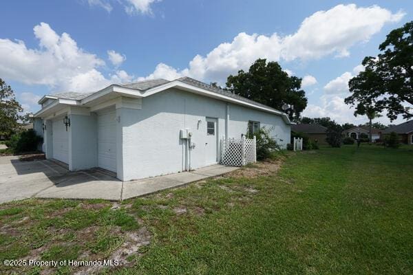 4048 St Ives Blvd, Spring Hill, FL 34609 - view of side of home with concrete driveway, a lawn, an attached garage, and stucco siding