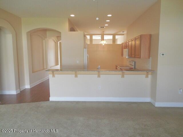 kitchen featuring carpet flooring, a kitchen breakfast bar, a peninsula, white microwave, and recessed lighting