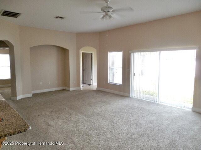 unfurnished living room featuring arched walkways, a ceiling fan, carpet, and baseboards