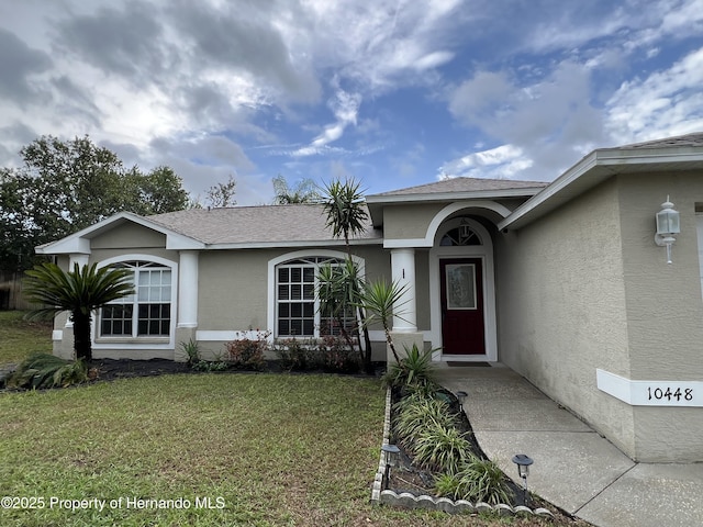 10448 Canary Ave, Weeki Wachee, FL 34613 - view of front of house with stucco siding, a front yard, and a shingled roof