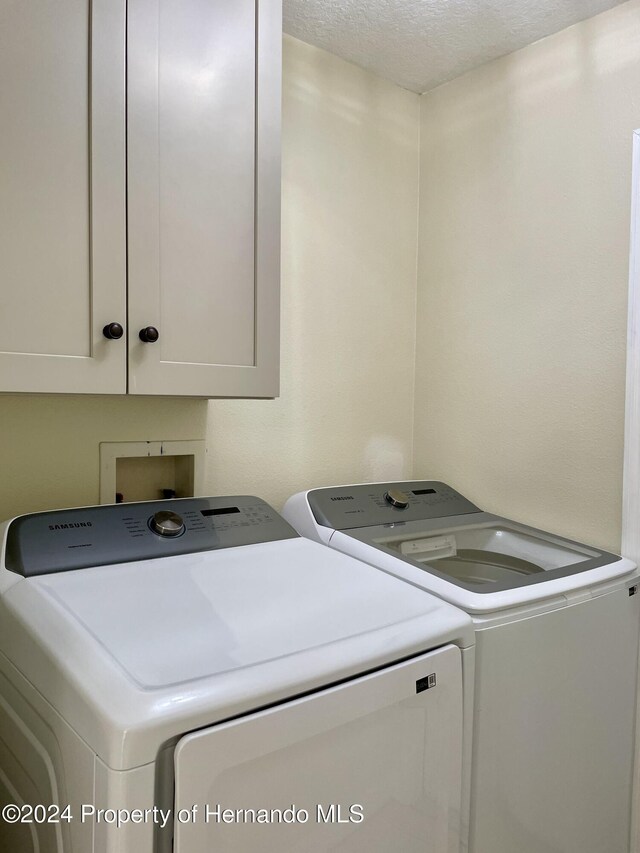 10448 Canary Ave, Weeki Wachee, FL 34613 - washroom featuring washing machine and clothes dryer, cabinet space, and a textured ceiling