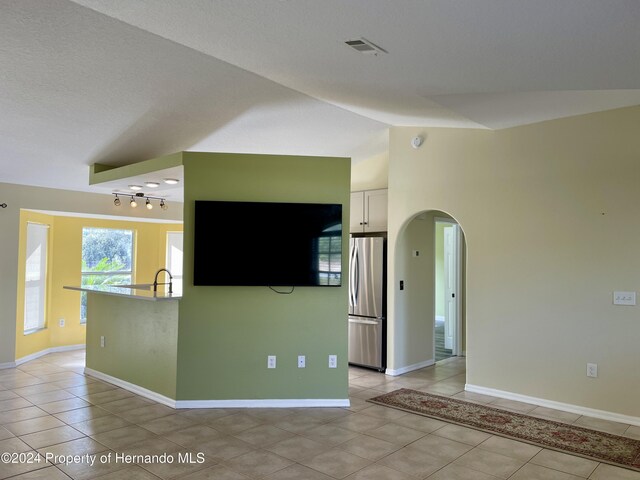10448 Canary Ave, Weeki Wachee, FL 34613 - kitchen with freestanding refrigerator, light tile patterned floors, arched walkways, rail lighting, and vaulted ceiling