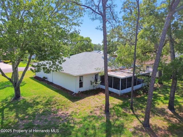 2183 Westchester Blvd, Spring Hill, FL 34606 - view of side of home with a sunroom, a lawn, a shingled roof, and stucco siding