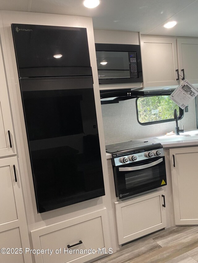 4035 Jason Rd, Spring Hill, FL 34608 - kitchen with black appliances, light wood-style floors, white cabinetry, and decorative backsplash