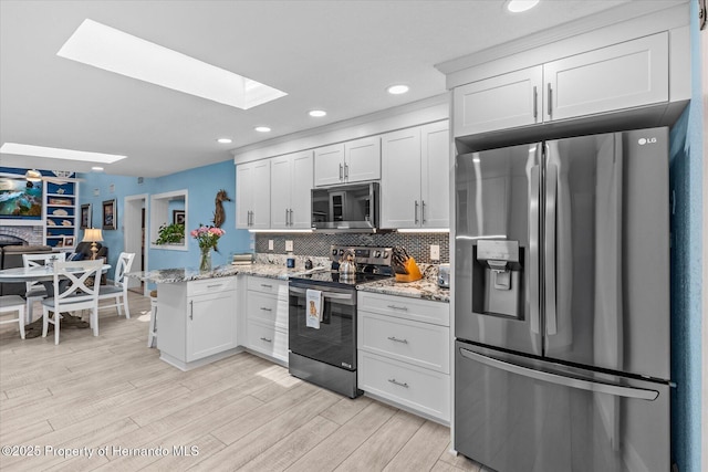 4387 6th Isle Dr, Hernando Beach, FL 34607 - kitchen featuring appliances with stainless steel finishes, a skylight, a peninsula, light wood-style floors, and backsplash