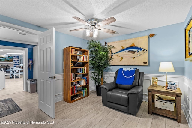 4387 6th Isle Dr, Hernando Beach, FL 34607 - sitting room featuring wood finished floors, ceiling fan, wainscoting, a textured ceiling, and a decorative wall