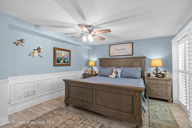 4387 6th Isle Dr, Hernando Beach, FL 34607 - bedroom with a textured ceiling, a wainscoted wall, light wood-style flooring, and a ceiling fan