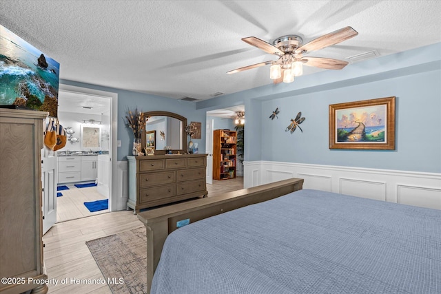 4387 6th Isle Dr, Hernando Beach, FL 34607 - bedroom with a walk in closet, a textured ceiling, wainscoting, light wood-type flooring, and connected bathroom