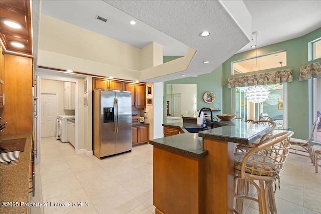9161 Southern Comfort Ct, Weeki Wachee, FL 34613 - kitchen with stainless steel fridge with ice dispenser, a sink, brown cabinetry, washer and dryer, and light tile patterned floors