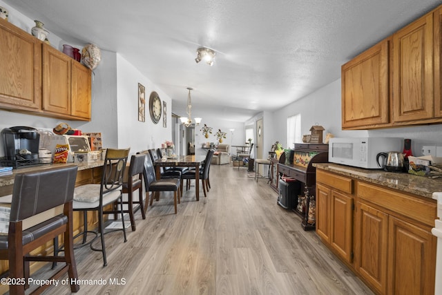 16040 Platinum Dr, Spring Hill Pasco, FL 34610 - kitchen featuring white microwave, light wood finished floors, brown cabinetry, dark stone countertops, and hanging light fixtures