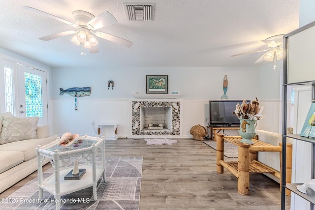 5507 Darlene St, Weeki Wachee, FL 34607 - living room featuring a ceiling fan, a tile fireplace, a wainscoted wall, wood finished floors, and a textured ceiling