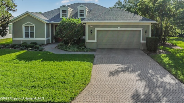 5233 Jennings Trl, Brooksville, FL 34601 - view of front of house featuring a front yard, decorative driveway, stucco siding, a garage, and roof with shingles