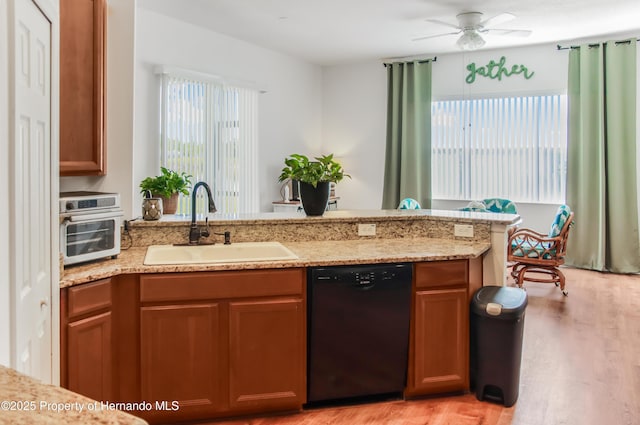 5233 Jennings Trl, Brooksville, FL 34601 - kitchen with black dishwasher, a sink, light wood-style flooring, light stone countertops, and a peninsula