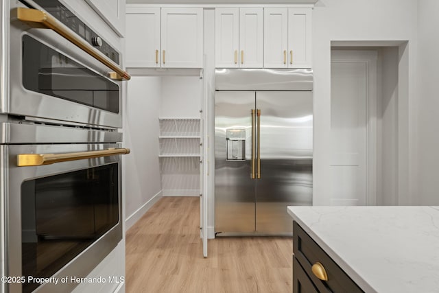 4522 Majestic Hills Loop, Brooksville, FL 34601 - kitchen with stainless steel appliances, light wood finished floors, white cabinetry, and light stone countertops