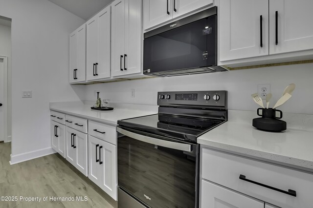 1080 Dunlap Ave, Spring Hill, FL 34609 - kitchen with range with electric cooktop, black microwave, light wood-style floors, and white cabinetry