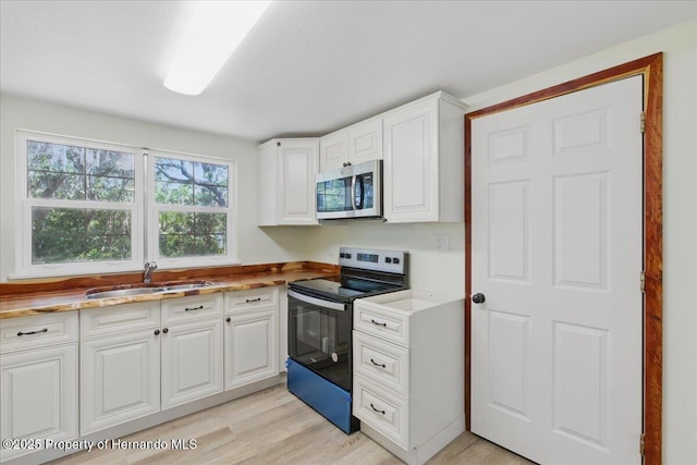 12301 Cedar St, Cedar Key, FL 32625 - kitchen featuring appliances with stainless steel finishes, a sink, light wood-style floors, and white cabinets