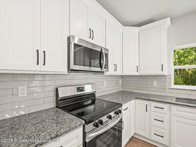 14448 Chimney Swift Rd, Weeki Wachee, FL 34614 - kitchen with appliances with stainless steel finishes, white cabinetry, dark stone countertops, and tasteful backsplash