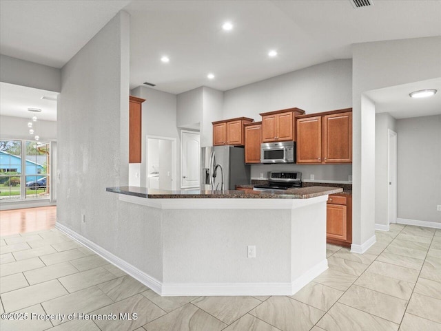 12167 Bath St, Spring Hill, FL 34609 - kitchen with appliances with stainless steel finishes, brown cabinetry, dark stone countertops, baseboards, and a peninsula