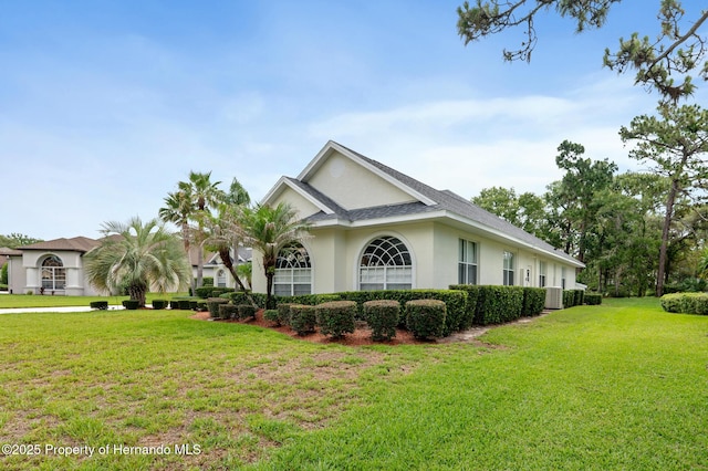 5182 Championship Cup Ln, Spring Hill, FL 34609 - view of front of property featuring a front lawn, stucco siding, central AC unit, and roof with shingles