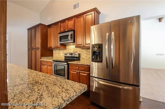 39127 Pretty Pond Rd, Zephyrhills, FL 33540 - kitchen with stainless steel appliances, backsplash, light stone countertops, brown cabinets, and lofted ceiling