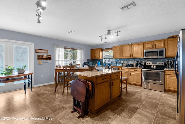 10457 Cranston St, Spring Hill, FL 34608 - kitchen with appliances with stainless steel finishes, rail lighting, tasteful backsplash, a kitchen island, and a breakfast bar