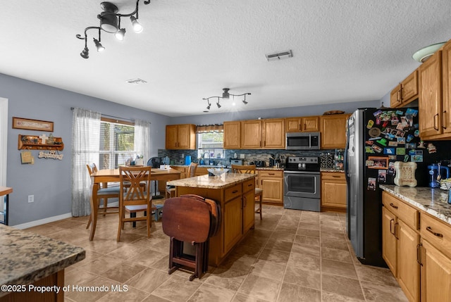10457 Cranston St, Spring Hill, FL 34608 - kitchen featuring stainless steel appliances, a kitchen island, decorative backsplash, light stone countertops, and a textured ceiling