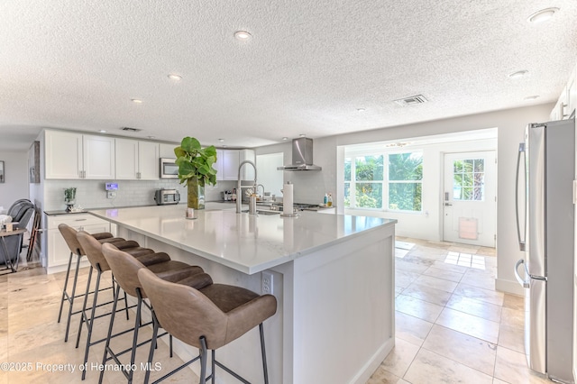 4566 Gulfstream Dr, Hernando Beach, FL 34607 - kitchen featuring stainless steel appliances, wall chimney range hood, white cabinetry, decorative backsplash, and a kitchen breakfast bar