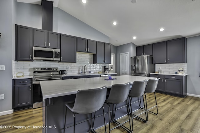 4123 Daisy Dr, Hernando Beach, FL 34607 - kitchen with appliances with stainless steel finishes, a kitchen bar, wood finished floors, lofted ceiling, and backsplash