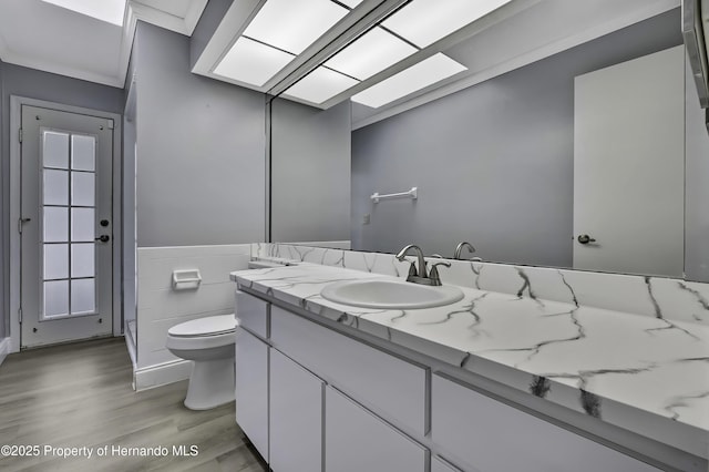 10277 Rosetti Ct, Spring Hill, FL 34608 - bathroom with toilet, wood finished floors, vanity, a wainscoted wall, and tile walls