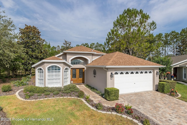 11404 Inman Ct, Spring Hill, FL 34609 - view of front of home with stucco siding, a garage, french doors, decorative driveway, and roof with shingles