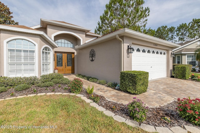11404 Inman Ct, Spring Hill, FL 34609 - view of front facade featuring stucco siding, an attached garage, decorative driveway, and french doors