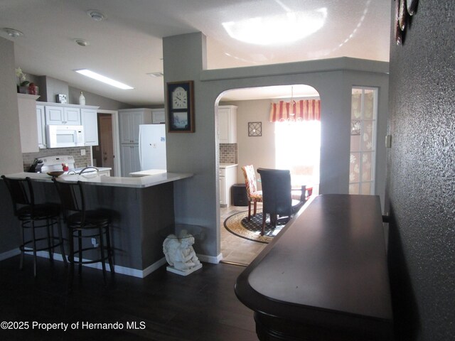 8423 Dickens Ave, Brooksville, FL 34613 - kitchen with white appliances, tasteful backsplash, arched walkways, white cabinetry, and wood finished floors