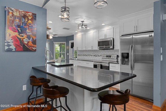 2295 Rio Cir, Spring Hill, FL 34608 - kitchen featuring appliances with stainless steel finishes, decorative backsplash, a breakfast bar area, white cabinetry, and a peninsula