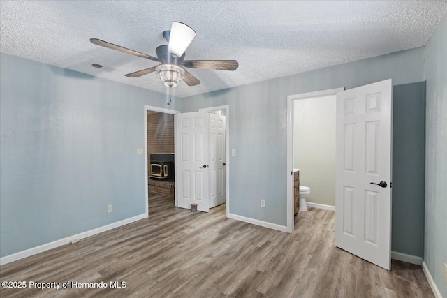 1518 Palm St, Steinhatchee, FL 32359 - unfurnished bedroom with wood finished floors, a textured ceiling, a wood stove, connected bathroom, and a ceiling fan