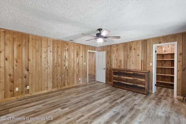 1518 Palm St, Steinhatchee, FL 32359 - unfurnished bedroom featuring a textured ceiling, wood finished floors, wood walls, a ceiling fan, and a walk in closet