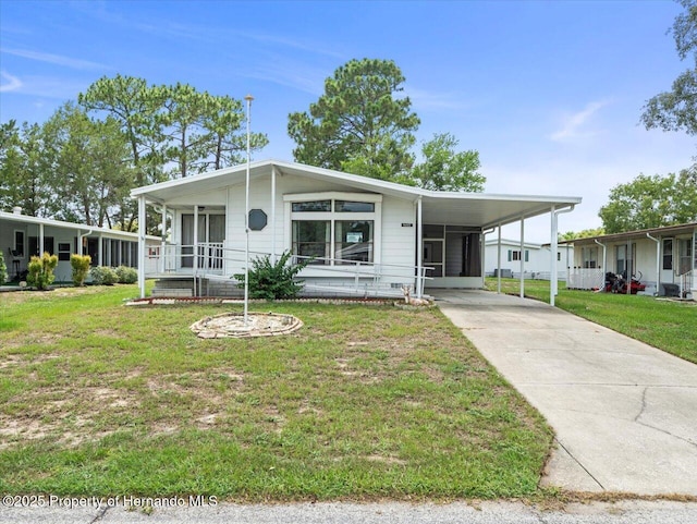 8017 Fiat Ave, Brooksville, FL 34613 - manufactured / mobile home featuring concrete driveway, a front yard, a carport, and a sunroom