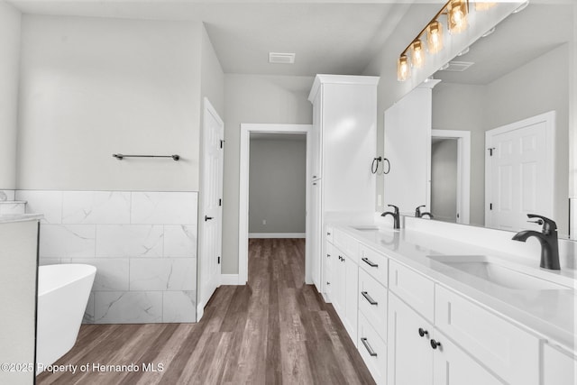 16113 Penn State Rd, Weeki Wachee, FL 34614 - full bathroom featuring double vanity, wood finished floors, a soaking tub, tile walls, and a wainscoted wall