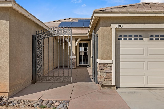 exterior space featuring solar panels, a tile roof, a gate, an attached garage, and stucco siding