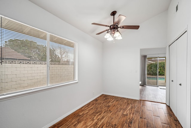 empty room with wood finished floors, visible vents, baseboards, ceiling fan, and vaulted ceiling