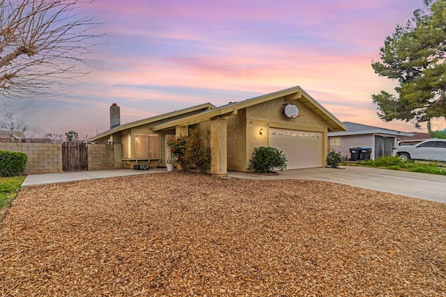 view of front of property with stucco siding, a garage, concrete driveway, and fence