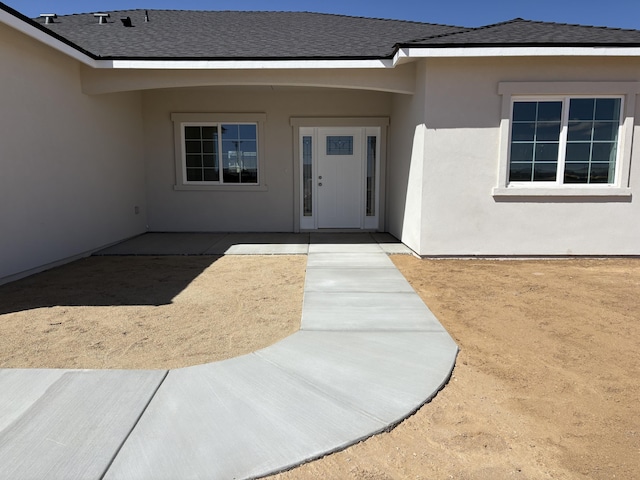 entrance to property featuring stucco siding and roof with shingles