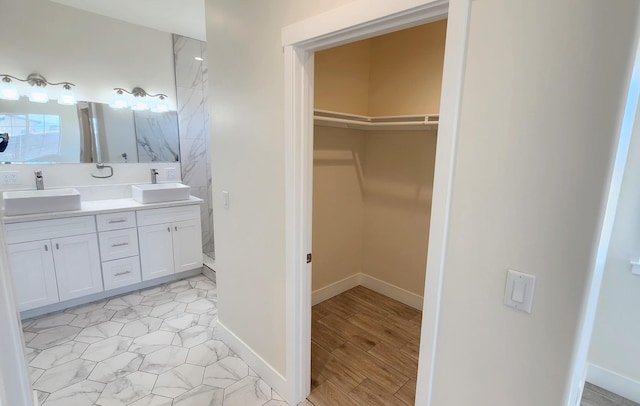 full bathroom with double vanity, a sink, a walk in closet, and baseboards