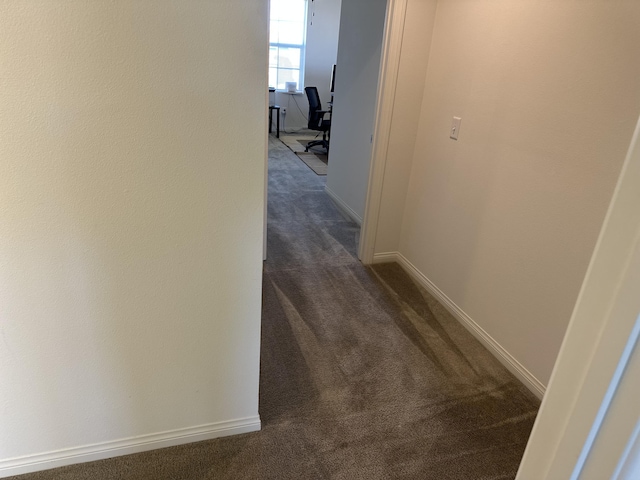 corridor featuring dark carpet and baseboards