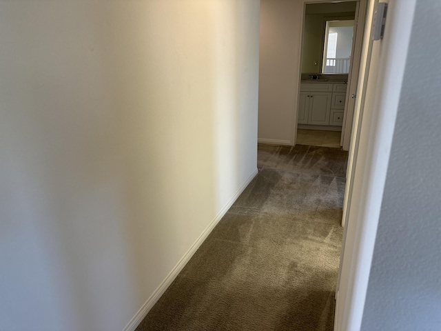 hallway with baseboards, dark carpet, and a sink