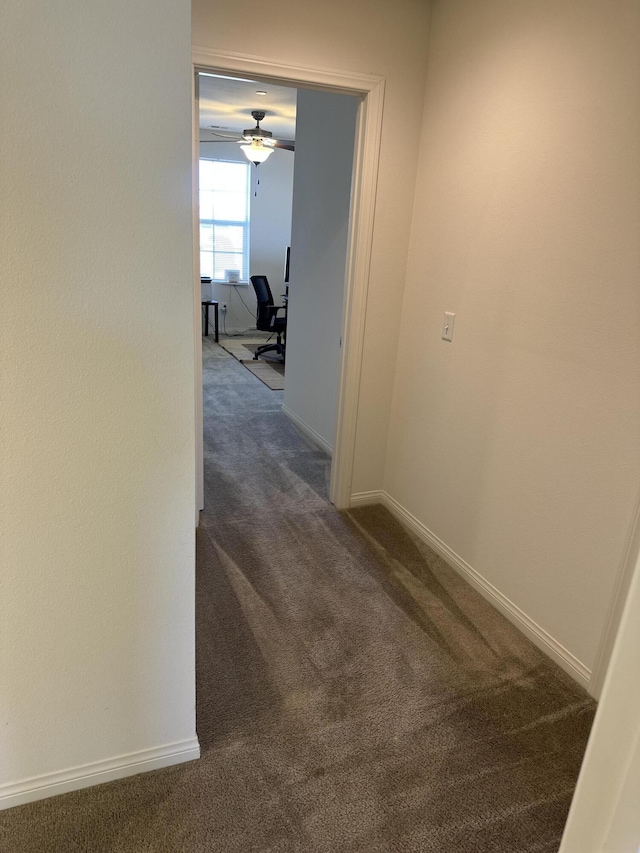 corridor featuring baseboards and dark carpet