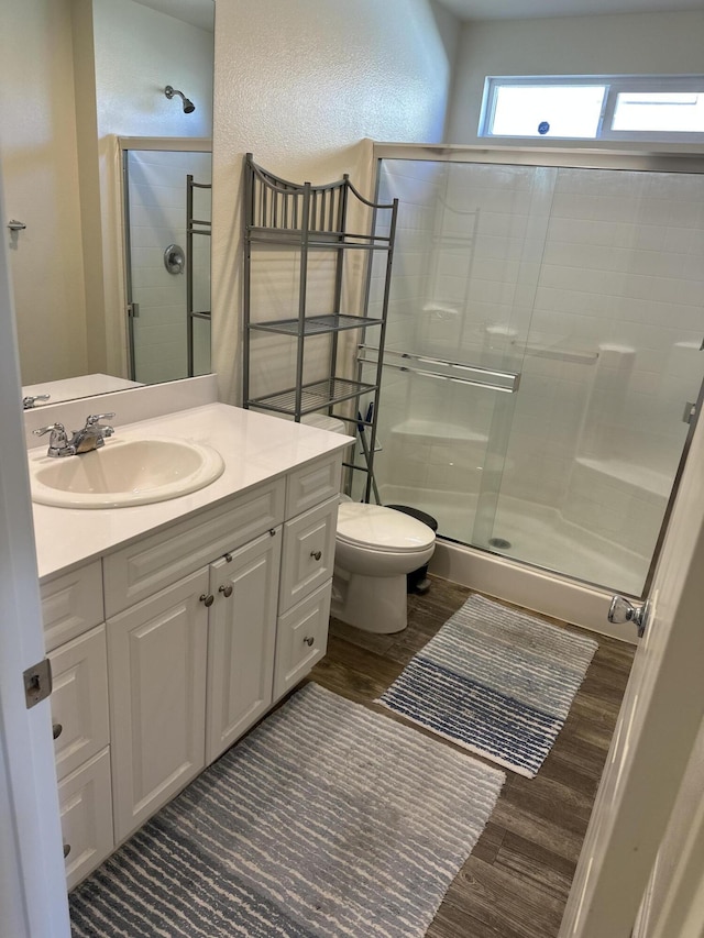 full bathroom with vanity, wood finished floors, a stall shower, toilet, and a textured wall