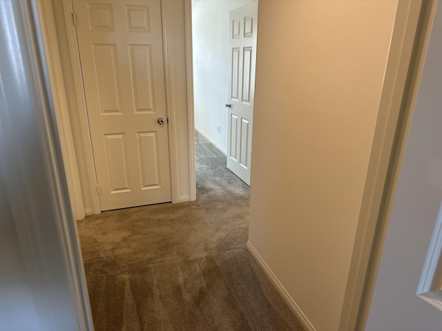 hall with baseboards and dark colored carpet