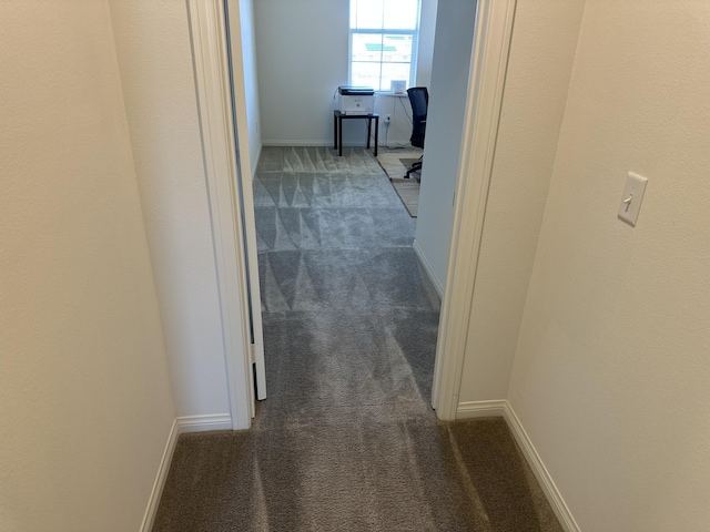 hallway with baseboards and dark carpet